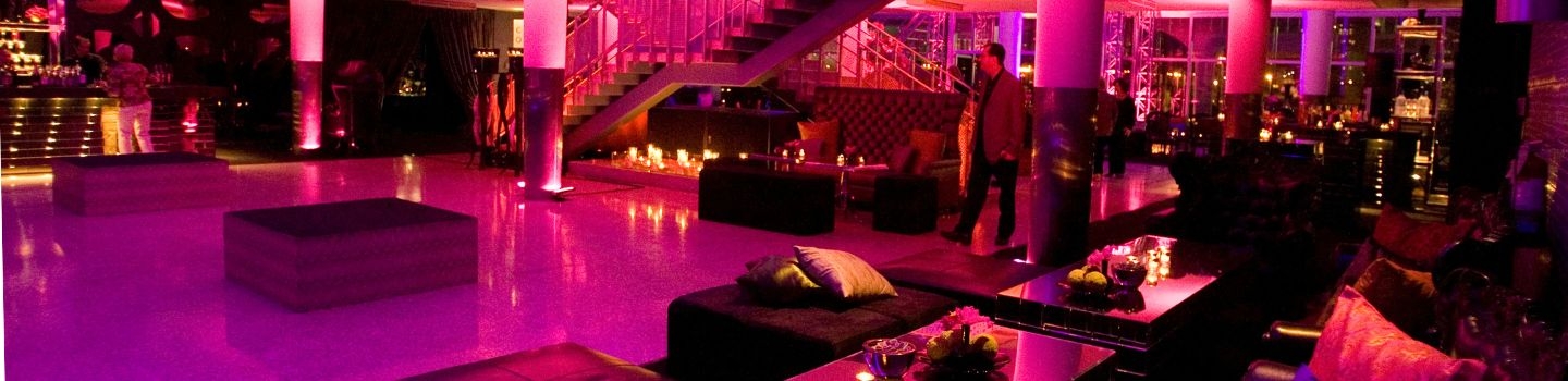 Pink-lit nightclub interior with bar, seating, and staircase.